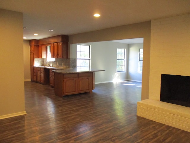 kitchen with kitchen peninsula, dark hardwood / wood-style flooring, tasteful backsplash, and a fireplace