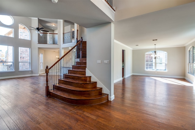 stairs with crown molding, wood-type flooring, and ceiling fan with notable chandelier