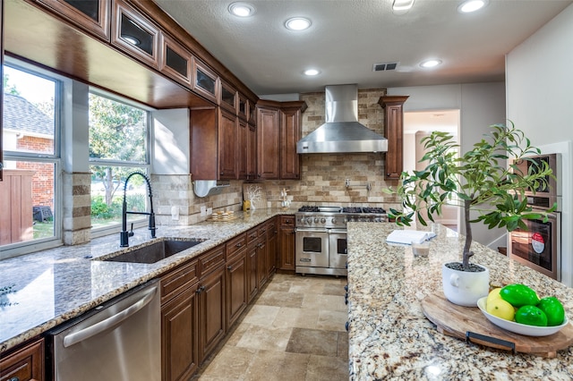 kitchen with stainless steel appliances, a sink, visible vents, backsplash, and wall chimney exhaust hood