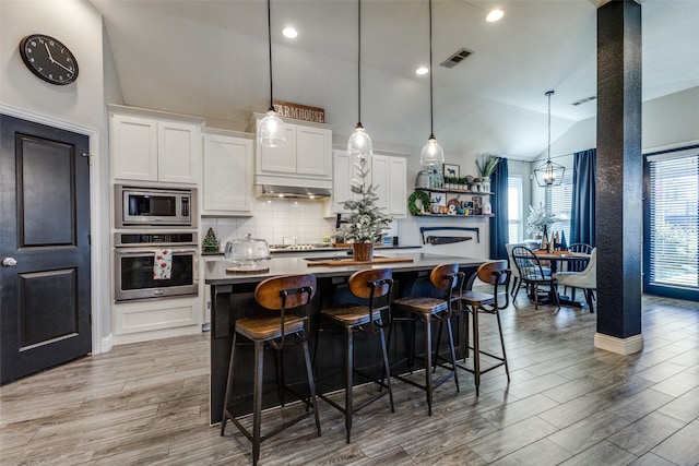 kitchen with stainless steel appliances, a center island with sink, white cabinetry, hanging light fixtures, and lofted ceiling