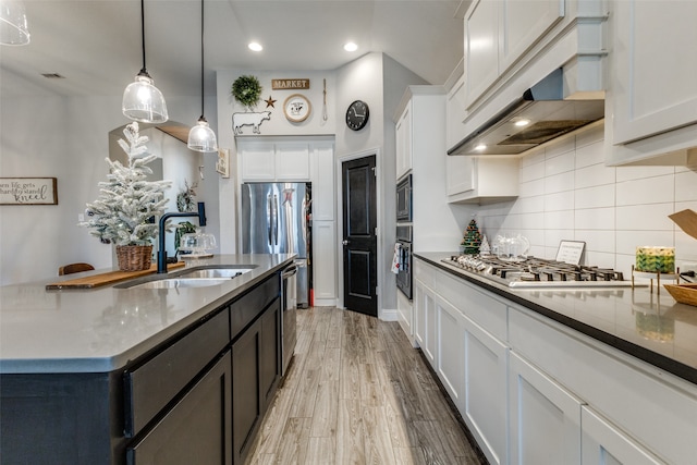 kitchen featuring light wood-type flooring, stainless steel appliances, sink, white cabinetry, and hanging light fixtures