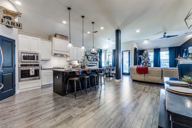 kitchen with white cabinetry, a kitchen island with sink, decorative light fixtures, and appliances with stainless steel finishes