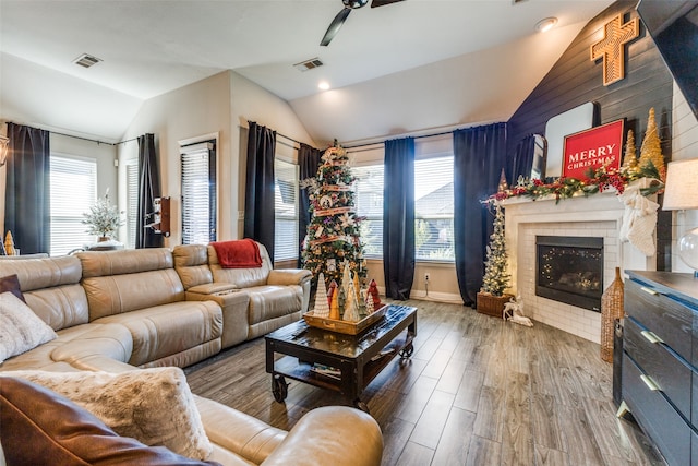 living room featuring lofted ceiling, a tile fireplace, wooden walls, ceiling fan, and wood-type flooring