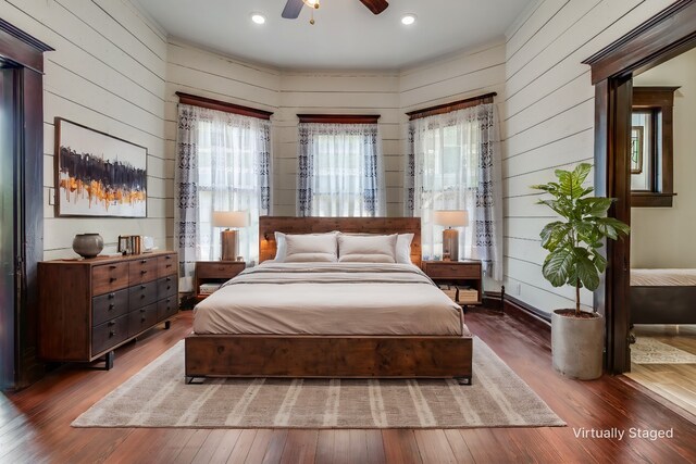 bedroom with multiple windows, ceiling fan, wooden walls, and dark wood-type flooring