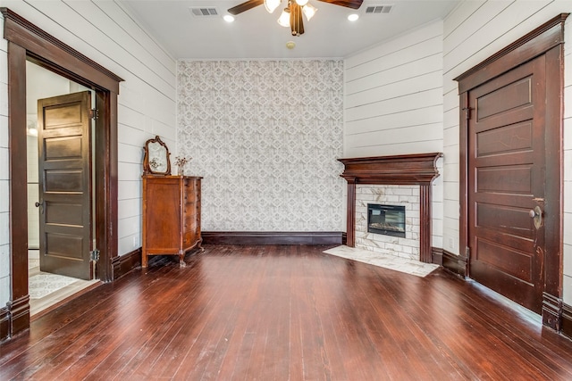 unfurnished living room featuring dark hardwood / wood-style floors, ceiling fan, and a stone fireplace