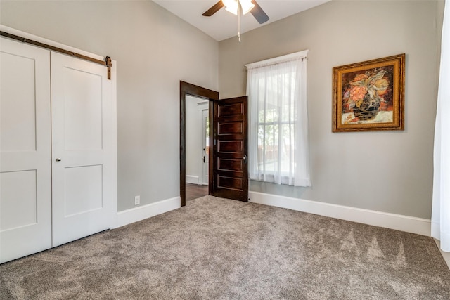 unfurnished bedroom with carpet flooring, a barn door, ceiling fan, and a closet