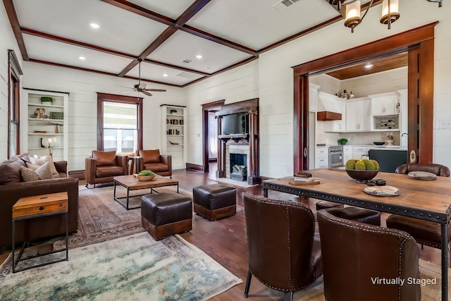 living room featuring coffered ceiling, ceiling fan, wood-type flooring, beamed ceiling, and a stone fireplace