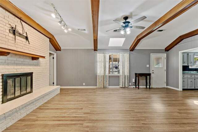 unfurnished living room featuring light wood-type flooring, a skylight, a brick fireplace, beam ceiling, and wood walls