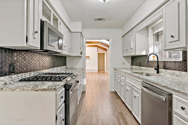 kitchen featuring appliances with stainless steel finishes, light stone counters, sink, white cabinets, and light hardwood / wood-style floors