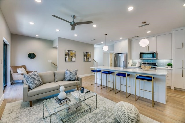 living room with ceiling fan, sink, and light hardwood / wood-style floors