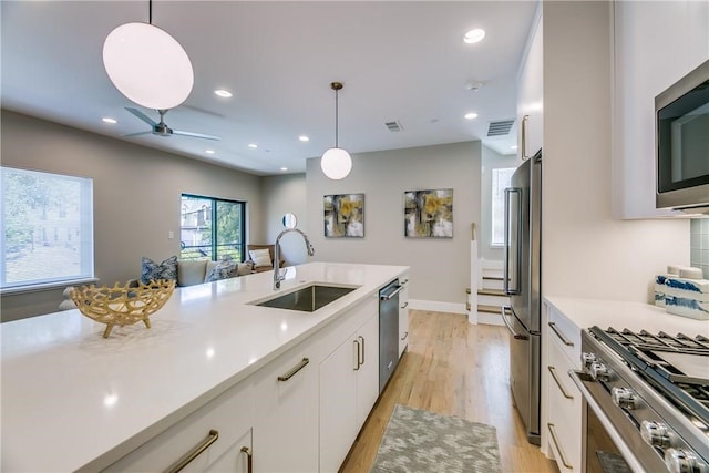 kitchen with stainless steel appliances, sink, decorative light fixtures, light hardwood / wood-style floors, and white cabinetry