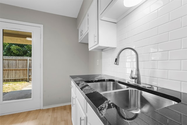 kitchen with white cabinetry, sink, tasteful backsplash, light hardwood / wood-style flooring, and dark stone counters