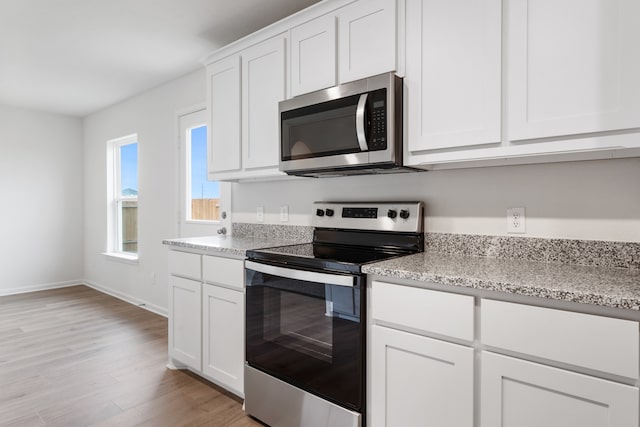 kitchen with white cabinets, light stone countertops, light wood-type flooring, and appliances with stainless steel finishes