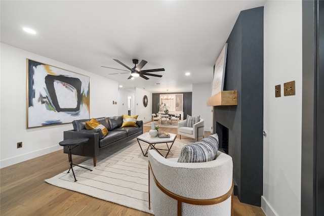 living room with a fireplace, hardwood / wood-style floors, and ceiling fan with notable chandelier