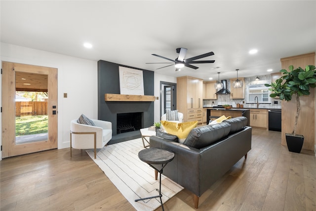 living room with a fireplace, ceiling fan, sink, and light hardwood / wood-style floors