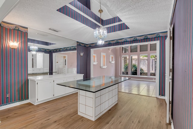 kitchen featuring white cabinetry, a center island, light hardwood / wood-style flooring, a chandelier, and a textured ceiling