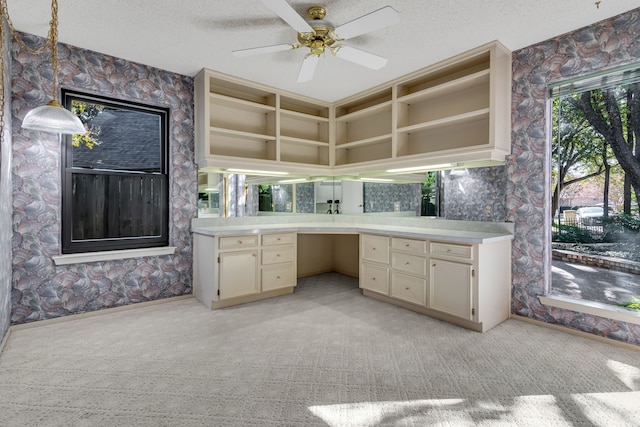 kitchen with ceiling fan, cream cabinetry, pendant lighting, light colored carpet, and a textured ceiling