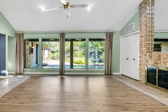 unfurnished living room featuring a brick fireplace, a textured ceiling, ceiling fan, hardwood / wood-style floors, and lofted ceiling