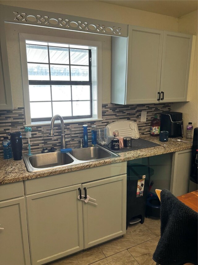 kitchen featuring backsplash, sink, light stone countertops, light tile patterned flooring, and white cabinetry