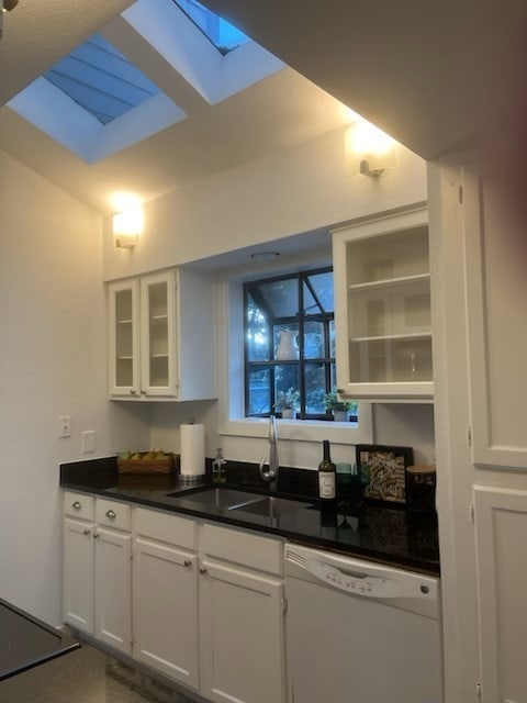 kitchen with a skylight, dishwasher, white cabinets, and sink