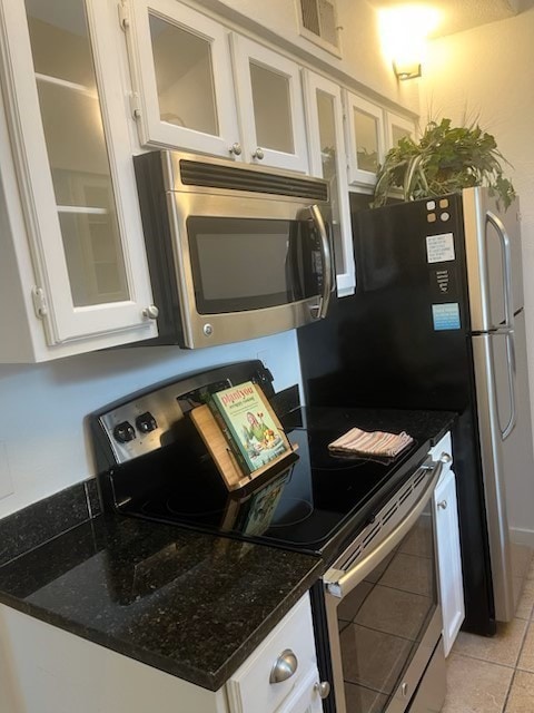 kitchen with white cabinets, appliances with stainless steel finishes, light tile patterned floors, and dark stone counters