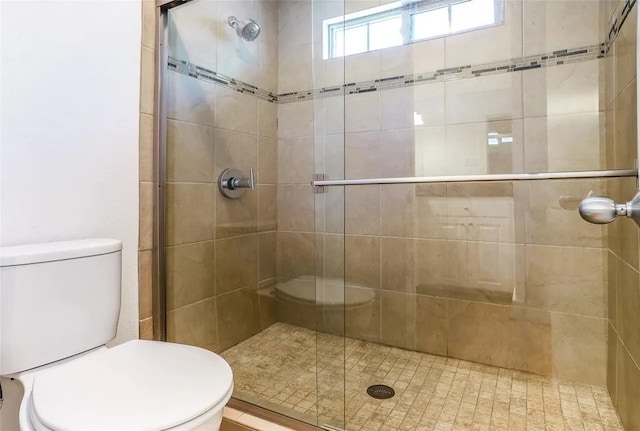 bathroom featuring a shower with door and toilet