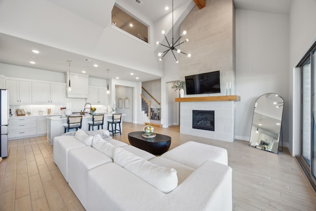 living room with sink, light hardwood / wood-style flooring, high vaulted ceiling, a notable chandelier, and a fireplace