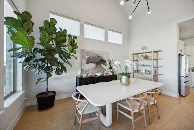 dining area with light wood-type flooring, high vaulted ceiling, and a notable chandelier