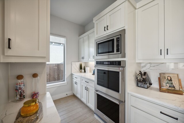 kitchen featuring light hardwood / wood-style flooring, light stone countertops, appliances with stainless steel finishes, tasteful backsplash, and white cabinetry