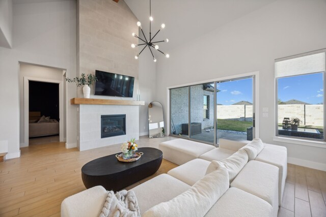 living room featuring a fireplace, high vaulted ceiling, a notable chandelier, and light hardwood / wood-style flooring