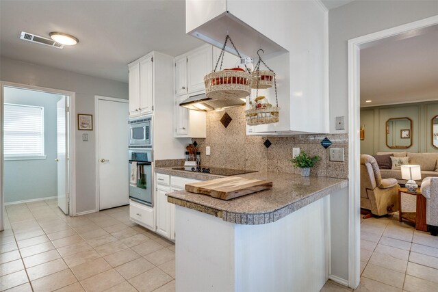 kitchen featuring kitchen peninsula, appliances with stainless steel finishes, backsplash, light tile patterned floors, and white cabinetry