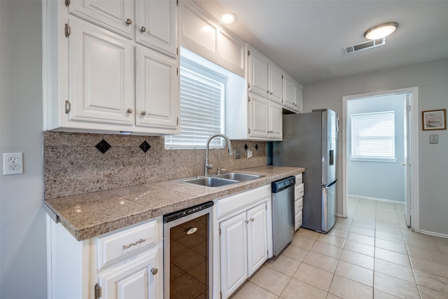 kitchen featuring sink, beverage cooler, tasteful backsplash, white cabinets, and appliances with stainless steel finishes