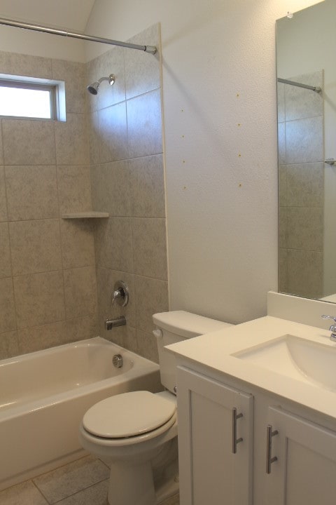 full bathroom featuring tile patterned flooring, lofted ceiling, toilet, vanity, and tiled shower / bath