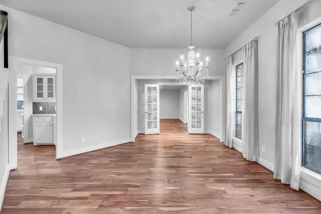 unfurnished dining area featuring a chandelier, light wood-type flooring, and french doors