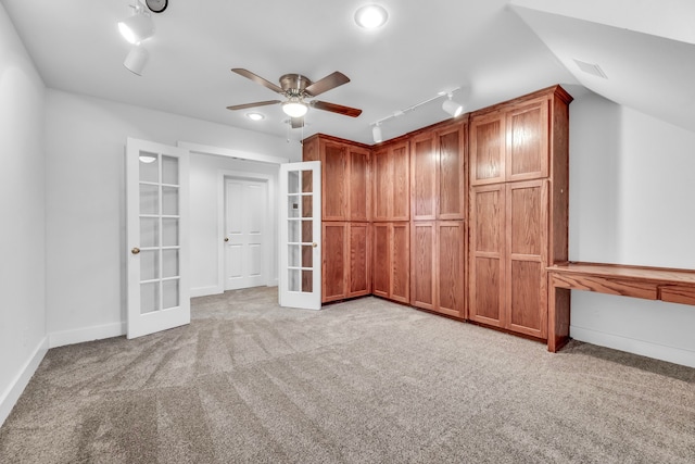 interior space featuring french doors, rail lighting, light colored carpet, and vaulted ceiling