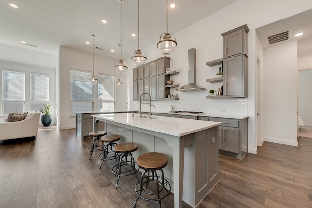 kitchen featuring dark wood-type flooring, ventilation hood, a kitchen breakfast bar, a center island with sink, and hanging light fixtures