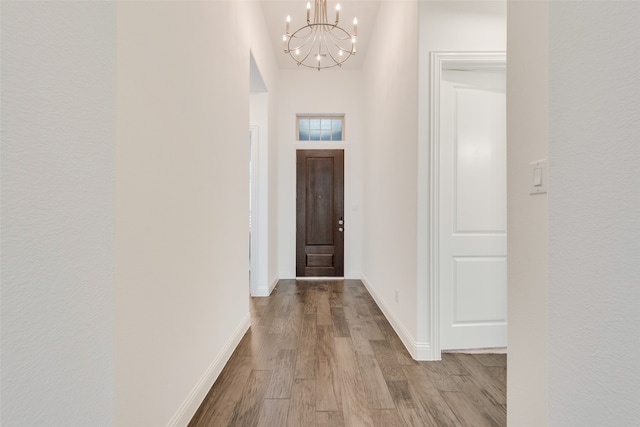 hall featuring a towering ceiling, light wood-type flooring, and an inviting chandelier