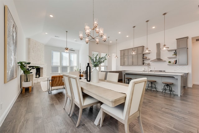 dining space with ceiling fan with notable chandelier, wood-type flooring, and a fireplace