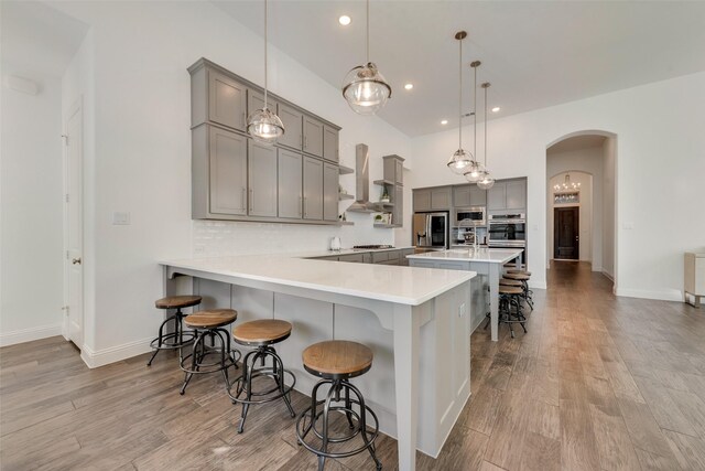 kitchen with pendant lighting, wall chimney exhaust hood, kitchen peninsula, a breakfast bar area, and stainless steel appliances