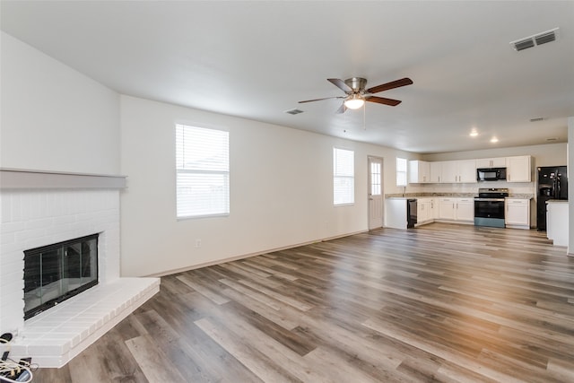 unfurnished living room with a brick fireplace, ceiling fan, a healthy amount of sunlight, and light wood-type flooring