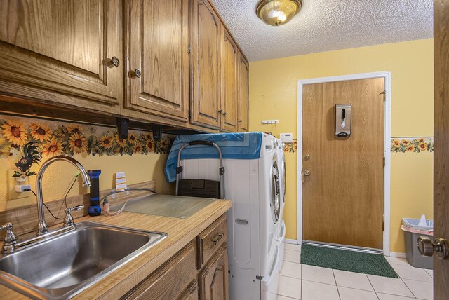 laundry room with washer and clothes dryer, cabinets, sink, light tile patterned floors, and a textured ceiling