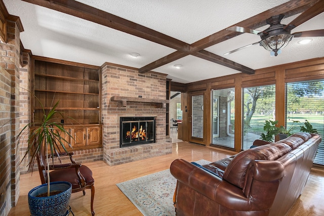 living room featuring beam ceiling, ceiling fan, a brick fireplace, light hardwood / wood-style floors, and a textured ceiling