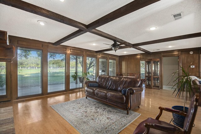 living room featuring beamed ceiling, wood walls, light wood-type flooring, and a textured ceiling