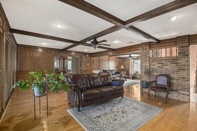 living room featuring beam ceiling, light hardwood / wood-style floors, a textured ceiling, and wooden walls