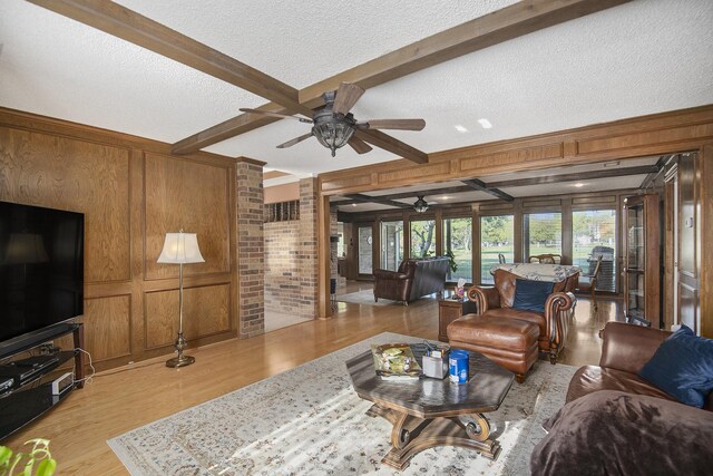 living room with wooden walls, ceiling fan, a textured ceiling, beam ceiling, and light hardwood / wood-style floors