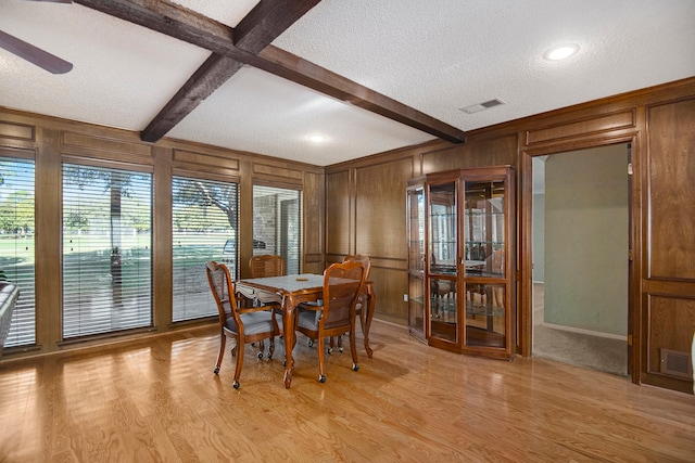 dining space featuring wood walls, light hardwood / wood-style floors, and beam ceiling