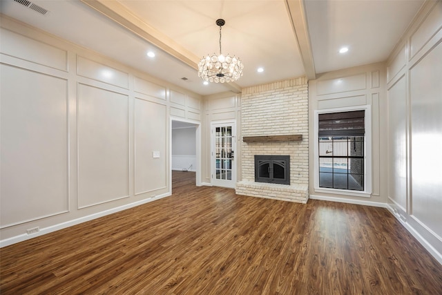 unfurnished living room with beamed ceiling, a brick fireplace, an inviting chandelier, and dark hardwood / wood-style flooring