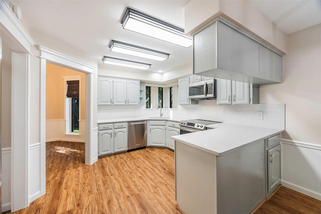 kitchen with stainless steel appliances, gray cabinets, light wood-type flooring, and kitchen peninsula