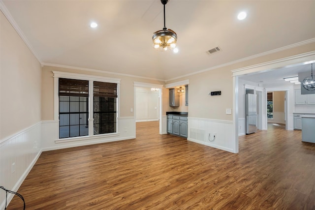 unfurnished living room featuring wood-type flooring, crown molding, and an inviting chandelier