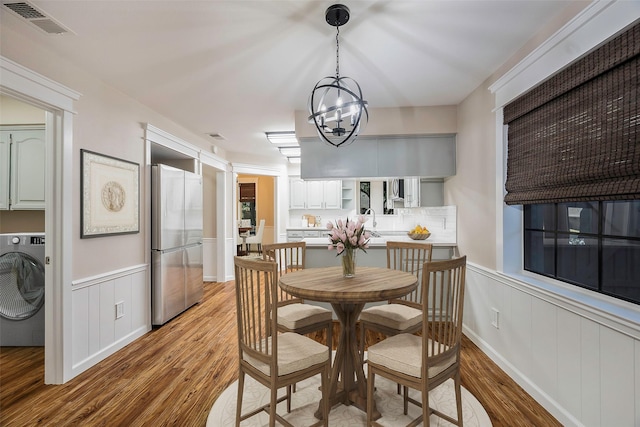 dining area featuring wood-type flooring, washer / dryer, and a notable chandelier